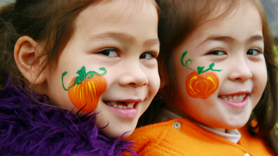 Two smiling children in Halloween costumes with pumpkins painted on their faces